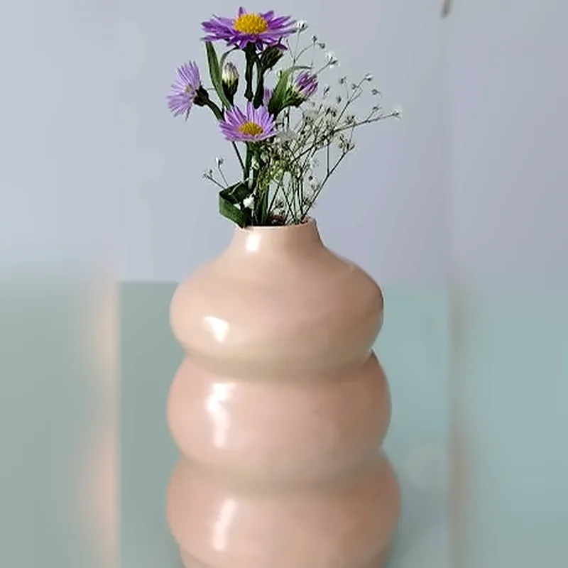 Florero rosa de cerámica en forma de donas apiladas con flores moradas