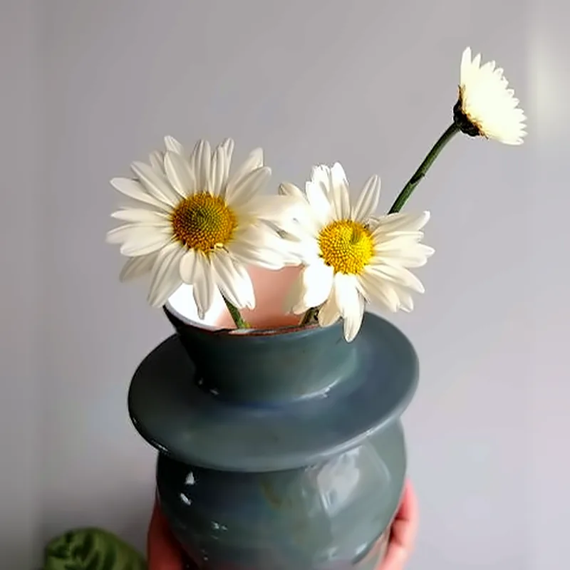 Florero de cerámica azul petróleo con un anillo al centro y margaritas
