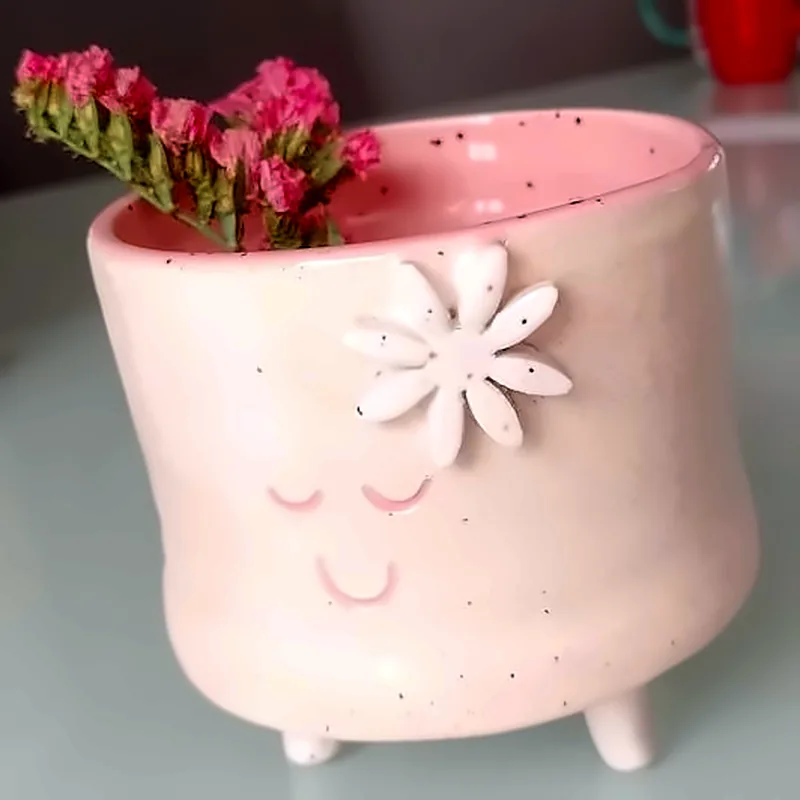 Maceta rosa de cerámica con carita sonriente, flor en relieve y flores secas