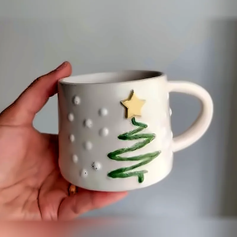 Taza blanca de cerámica con un pino verde y estrella dorada
