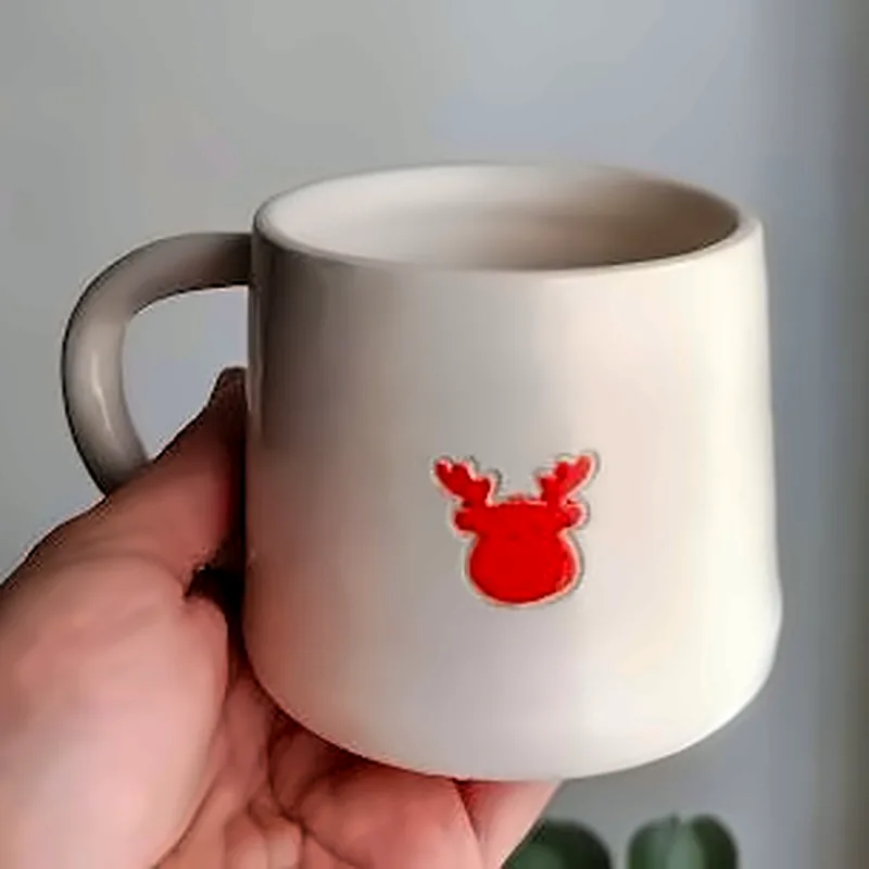 Taza blanca de cerámica con un reno rojo